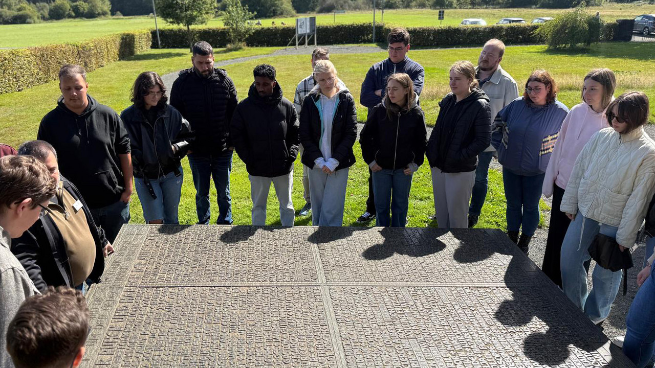 Studierende der Hochschule für öffentliche Verwaltung Rheinland-Pfalz und Georg Mertes stehen gemeinsam um den Gedenkstein in Hinzert und halten inne.