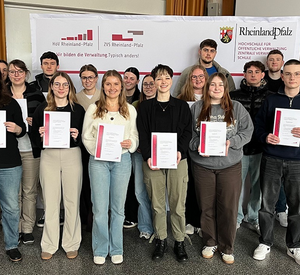 Design ohne Titel - 1 Gruppenfoto bei der Prämierung am 9. Februar 2026 an der HöV RLP: Direktorin Alice Schmidt steht links, in der Mitte die Preisträgerinnen und Preisträger der bestbewerteten Präsentation aus dem Hochschulforum Krisenmanagement 2026, Organisator und Dozent Christoph Buttner (2. v. r.). Mehrere Studierende halten Urkunden; vier ausgezeichnete Studierende sind nicht anwesend.