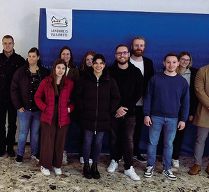 Studierendengruppe der Hochschule für öffentliche Verwaltung Rheinland-Pfalz mit Kämmerer Benedikt Friedrich (links) vor einer Pressewand in der Kreisverwaltung Vulkaneifel.