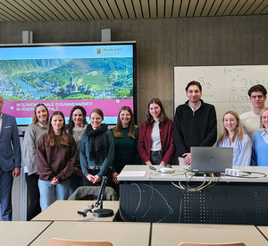 Gruppenfoto in einem Seminarraum an der HöV Rheinland-Pfalz. Die beiden Dozenten Thomas Schäfer und Ralf Schmorleiz stehen zusammen mit Dr. Andreas Rath und Kai Dommershausen vom Ministerium des Innern und für Sport Rheinland-Pfalz sowie den Studierenden des Wahlstudienfachs Interkommunale Zusammenarbeit. Alle blicken in die Kamera.