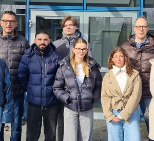 Acht Personen stehen bei sonnigem Wetter vor dem Eingang eines Gebäudes mit einem gelben Schild „INFORMATION“ über der Glastür. Es handelt sich um Studierende der Hochschule für öffentliche Verwaltung Rheinland-Pfalz am HIGIS-Zentrum in Hillesheim, einem Innovations- und Gründerzentrum der Verbandsgemeinde. 2. von links steht Stefan Mertes, Wirtschaftsförderer und Geschäftsführer des HIGIS-Zentrums, 2. von rechts steht Dr. Stefan Winggen, Dozent.