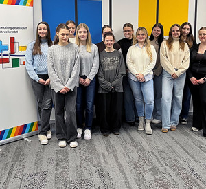 In einem Besprechungsraum steht eine Studierendengruppe der HöV RLP für ein Gruppenfoto zwischen Geschäftsführer Herbert Wiemer links und Dozent Christoph Buttner rechts vor einem Rollup der Aufbau- und Entwicklungsgesellschaft Bad Neuenahr-Ahrweiler mbH.