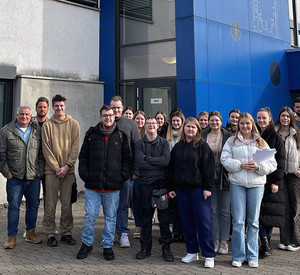 Gruppenfoto vor dem Eingang der Rhein-Mosel Werkstatt in Koblenz: Studierende und Dozent stehen draußen vor dem Gebäude.