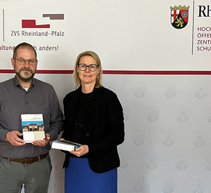  Zwei Personen stehen vor einer Pressewand mit dem Logo der Höv/ZVS Rheinland-Pfalz. Rechts im Bild steht die Direktorin Alice Schmidt und links steht der Dozent Thomas Schäfer. Beide lächeln in die Kamera und halten den Fachkommentar LandtagsWahlBrevier 2026 Kommentar zum Landtagswahlrecht Rheinland-Pfalz in den Händen.