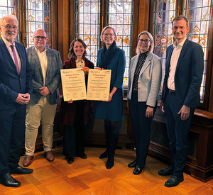 Gruppenfoto nach der Unterzeichnung der Kooperationsurkunden zwischen der Kommunal-Akademie Rheinland-Pfalz e. V. und der Hochschule für öffentliche Verwaltung Rheinland-Pfalz (HöV RLP) in der Villa Belgrano in Boppard. Von links nach rechts stehen Dr. Karl-Heinz Frieden, Stefan Heck, Eveline Breyer, Staatssekretärin Simone Schneider, Alice Schmidt und Michael Eckhardt. Eveline Breyer und Simone Schneider halten jeweils eine unterzeichnete Urkunde in den Händen.