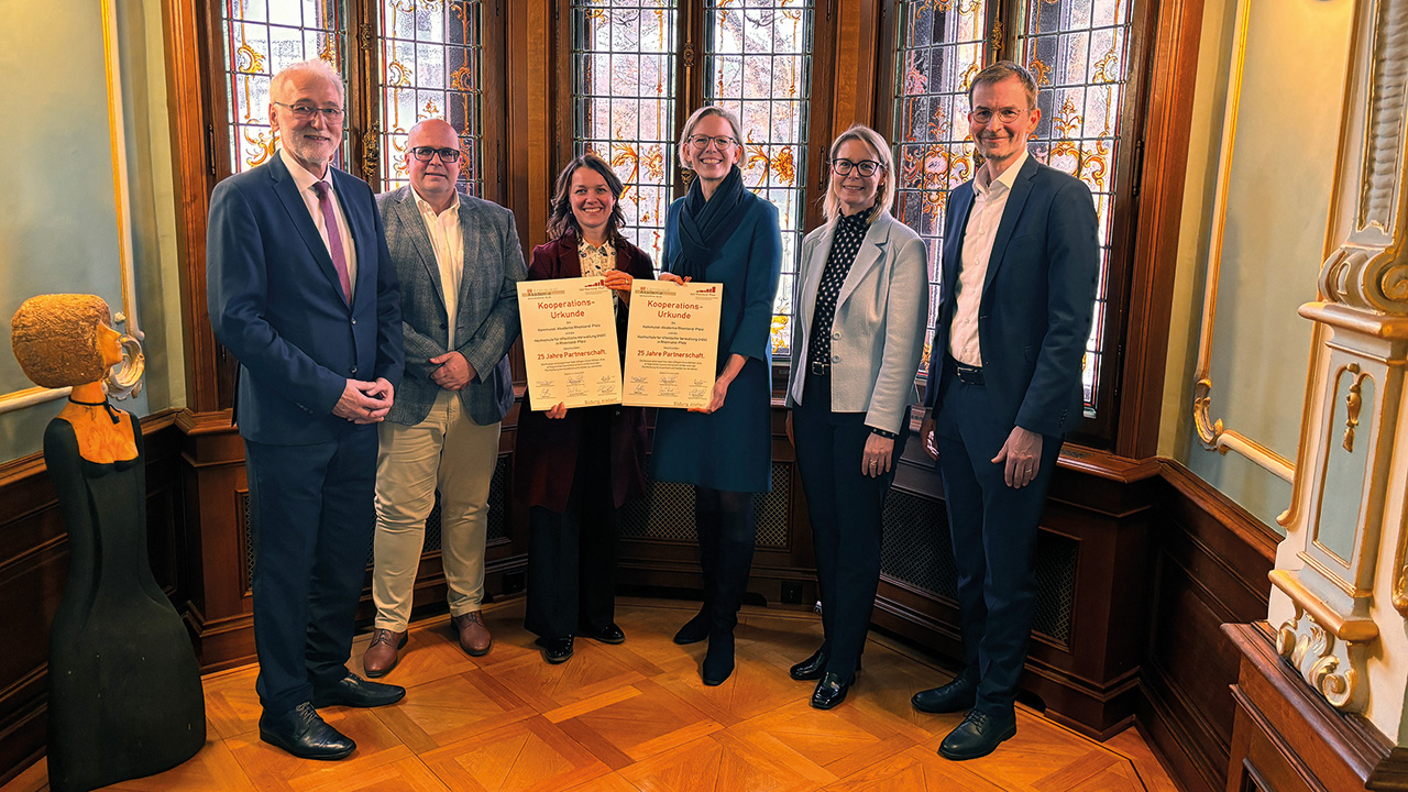Gruppenfoto nach der Unterzeichnung der Kooperationsurkunden zwischen der Kommunal-Akademie Rheinland-Pfalz e. V. und der Hochschule für öffentliche Verwaltung Rheinland-Pfalz (HöV RLP) in der Villa Belgrano in Boppard. Von links nach rechts stehen Dr. Karl-Heinz Frieden, Stefan Heck, Eveline Breyer, Staatssekretärin Simone Schneider, Alice Schmidt und Michael Eckhardt. Eveline Breyer und Simone Schneider halten jeweils eine unterzeichnete Urkunde in den Händen.