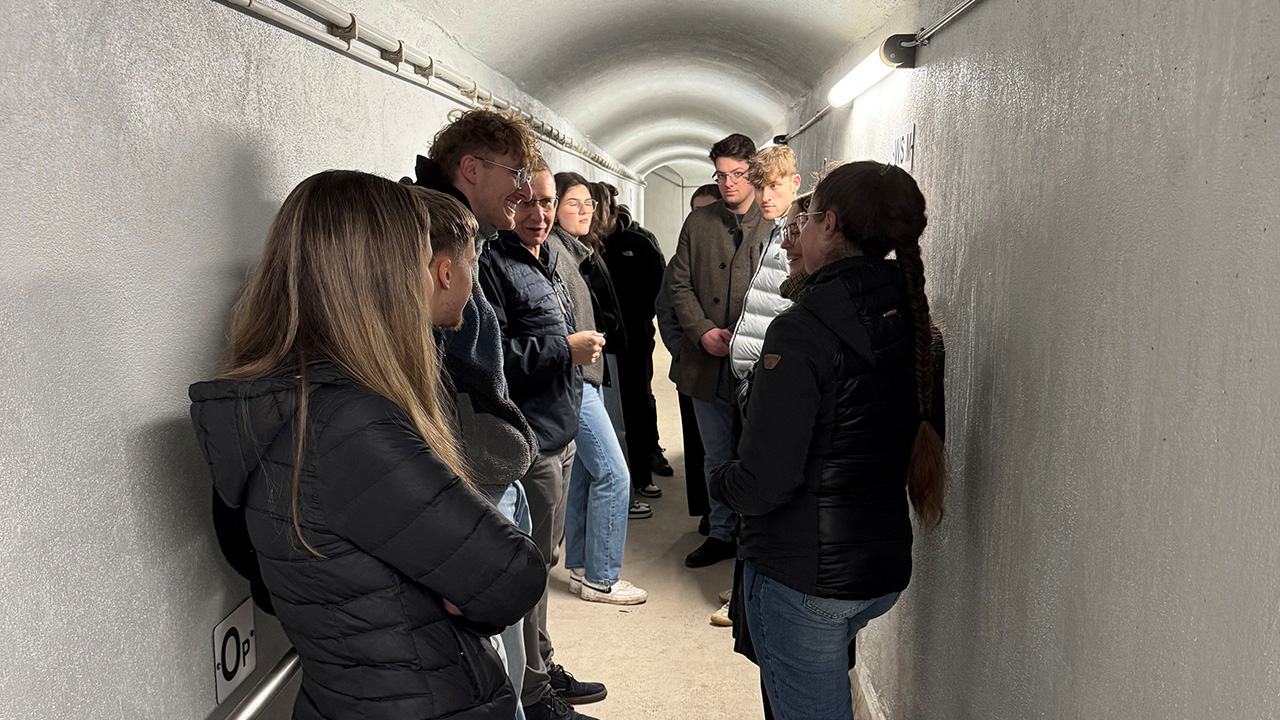 Mehrere Studierende stehen in einem schmalen, hell beleuchteten Kontrollstollen der Riveristalsperre und hören einer Erläuterung zur öffentlichen Wasserversorgung zu.