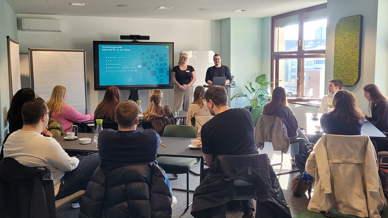 Sitzende Studierende hören in einem Seminarraum einem Vortrag von zwei Mitarbeitenden der KGSt zur Stellenbewertung im öffentlichen Dienst zu.