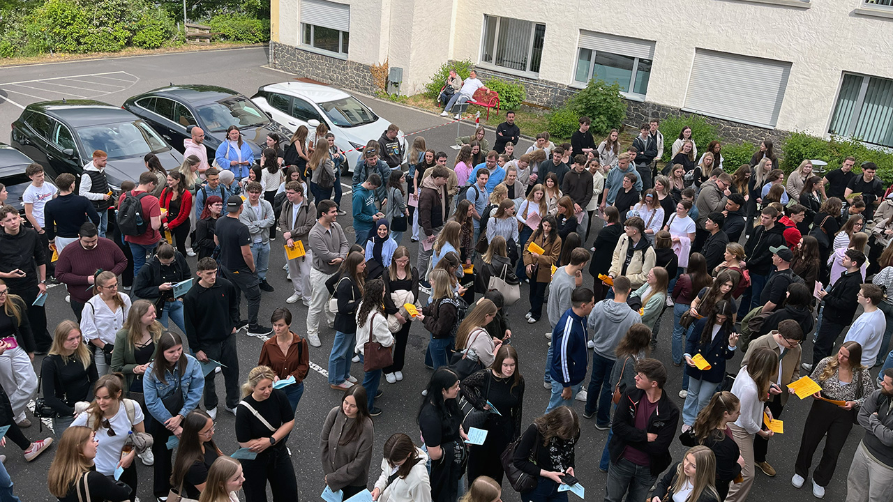 Viele Teilnehmende stehen mit Unterlagen im Innenhof der HöV RLP und ZVS RLP in Mayen. Sie warten in Gruppen vor einem Gebäude.